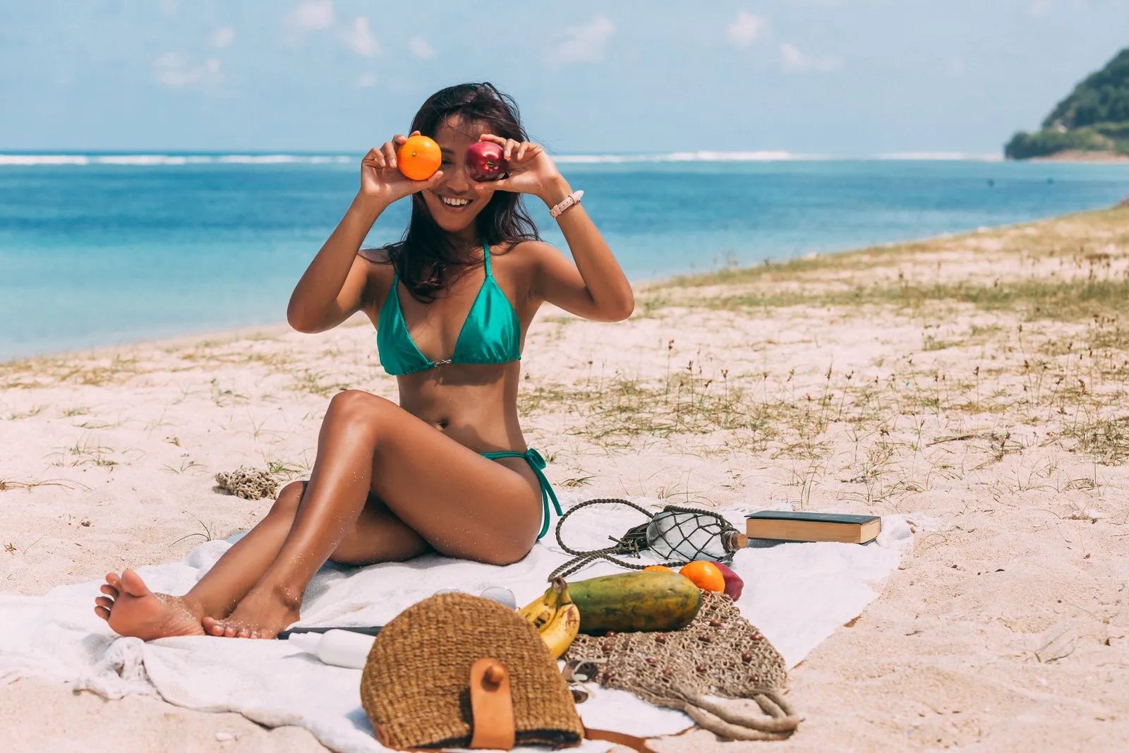 Woman enjoying a tropical beach picnic with fruits, sunbathing in a swimsuit by the sea.